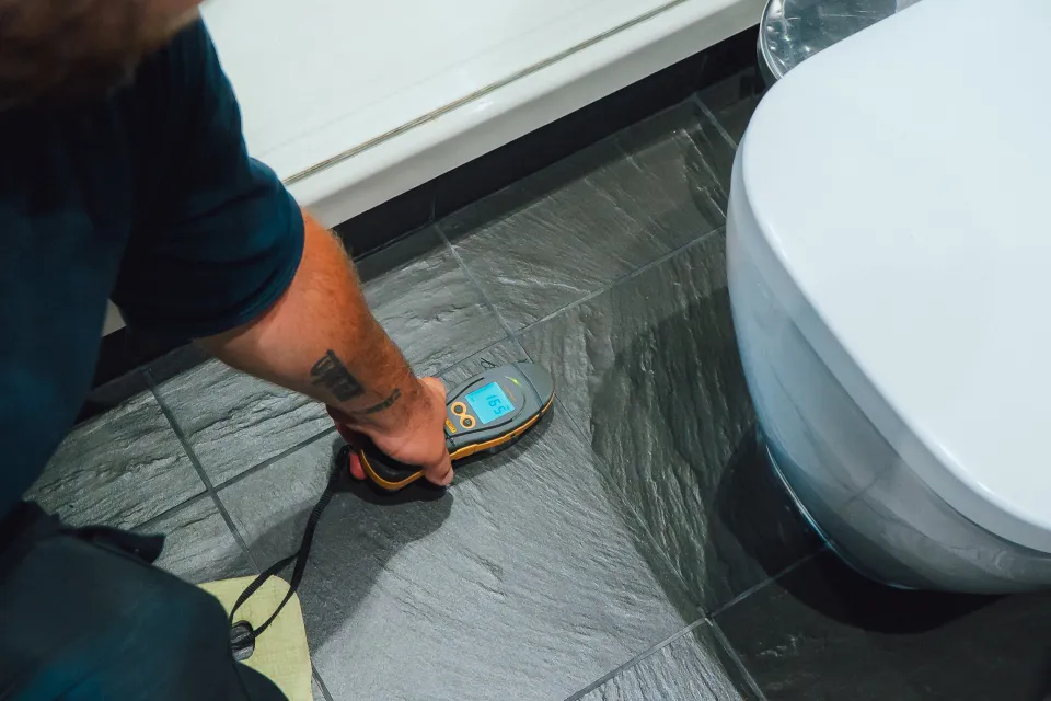 Moisture meter reading on a tiled bathroom floor next to a toilet